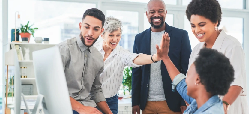 A diverse team of professionals celebrating success with high-fives in a modern office setting, symbolizing teamwork and achievement. The image reflects a positive work environment and collaboration, relevant to organizations pursuing ISO certification in UAE to enhance quality standards and employee engagement.